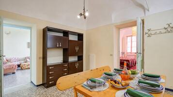 Un'area pranzo con un tavolo in legno apparecchiato per quattro persone, una panca e vista su una camera da letto con un letto e una finestra.