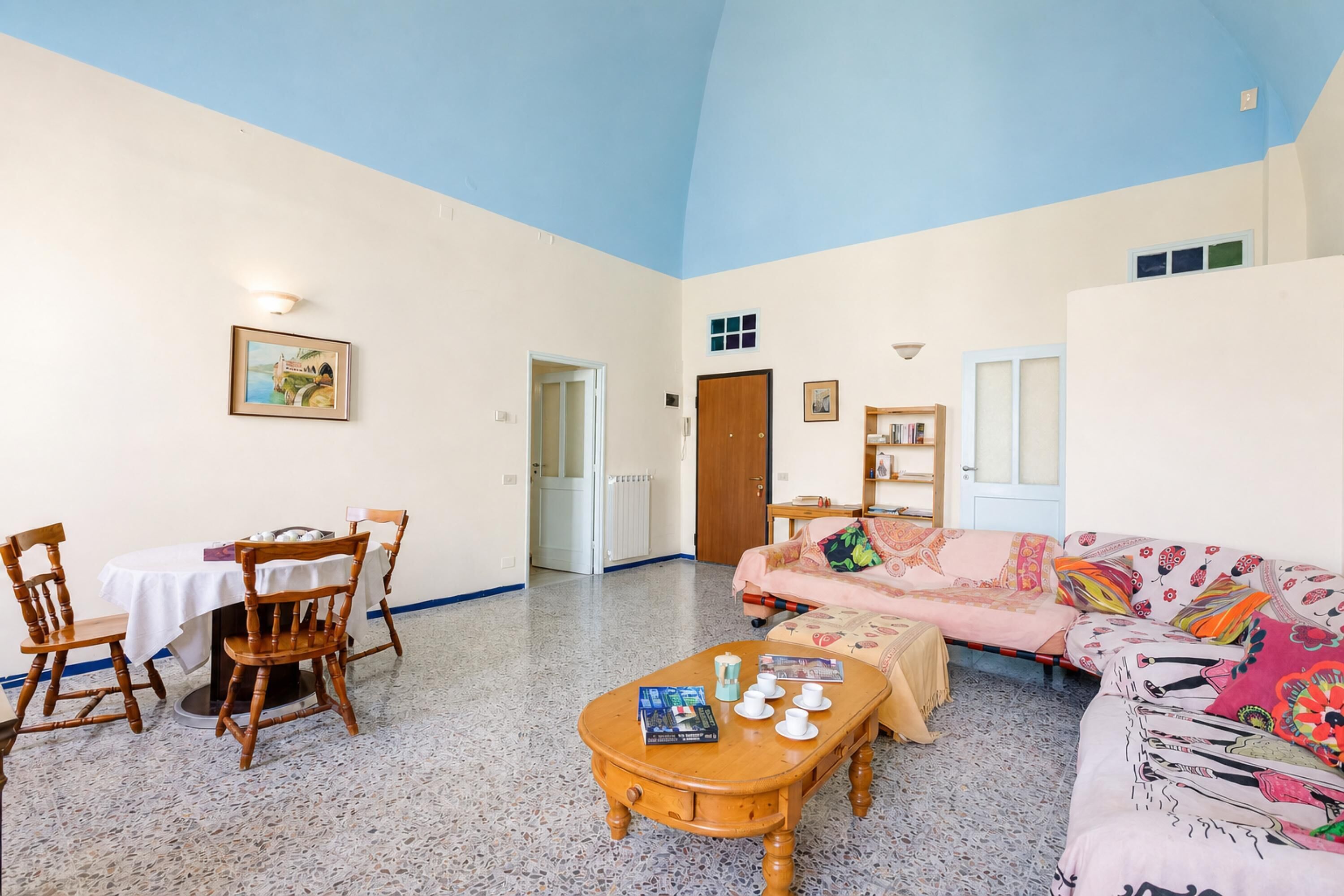 Un ampio soggiorno con soffitto alto, un'area pranzo con tavolo e sedie, un divano e un tavolino con libri e tazze.
