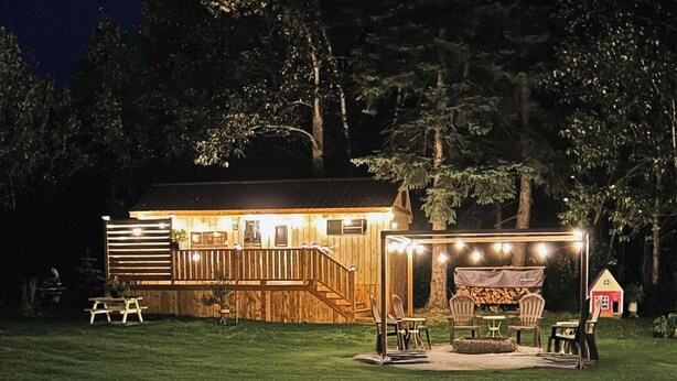 Une cabane en bois dotée d’une terrasse, de meubles d’extérieur et de guirlandes lumineuses.