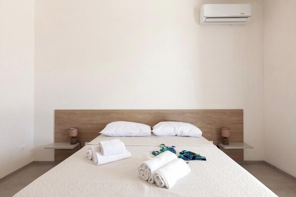 A hotel room with a bed, two pillows, a bedside table with a lamp, and a wall-mounted air conditioner. - Villa La Rimunda 1 Pool And Garden, Otranto, Italy (Otranto)