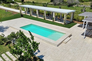 A rectangular swimming pool with a white deck, surrounded by a covered patio with chairs and a pergola. - Villa La Rimunda 1 Pool And Garden, Otranto, Italy (Otranto)