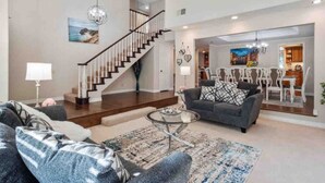 A spacious living room with a staircase, a grey sofa, and a dining area visible through an open doorway. - Secluded Romantic Getaway with Stunning NatureView (Anaheim)