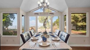 A dining room with a long table set for six, large windows, and a chandelier. - Secluded Romantic Getaway with Stunning NatureView (Anaheim)