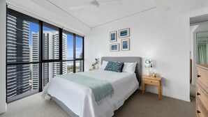 A modern bedroom with a large bed, a ceiling fan, and a view of high-rise buildings.