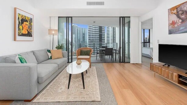 A modern living room with a grey sofa, a small white table, and a TV on a wooden stand.