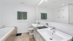 A modern bathroom with a bathtub, two sinks, a toilet, and a large mirror.