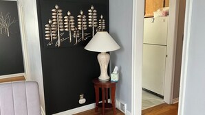 A room with a black accent wall, a white lamp on a wooden side table, and a visible door leading to a kitchen area. - 3BR home 20’ Dtn Detroit, near Corewell Health Hos, Meijer’s  Major Bus Routes (Detroit)