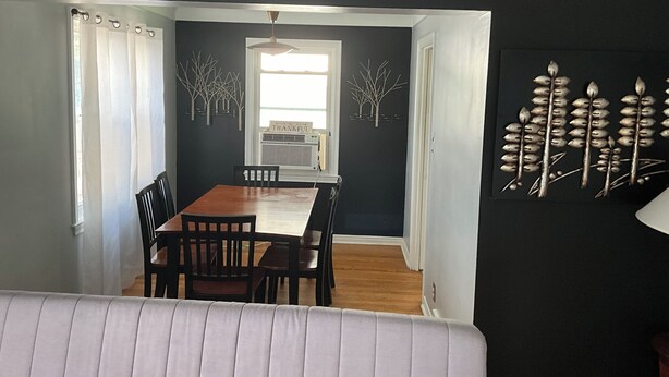 A dining area with a wooden table and chairs, a window with curtains, and a wall with decorative elements. - 3BR home 20’ Dtn Detroit, near Corewell Health Hos, Meijer’s  Major Bus Routes (Detroit)