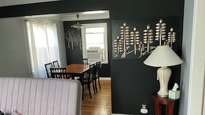 A room with a bed, a dining table with chairs, a wall-mounted lamp, and a wall decoration. - 3BR home 20’ Dtn Detroit, near Corewell Health Hos, Meijer’s  Major Bus Routes (Detroit)