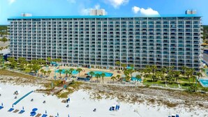 Ein großes Hotel mit mehreren Etagen, einem Poolbereich und einem Strand mit Liegestühlen.