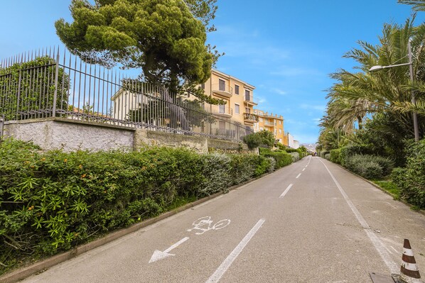 A road with a bicycle lane, bordered by a stone wall and metal fence, leading to a building with balconies. - Sunny House Spiagge e Ciclabile with Sea Views, Sanremo, Italy (Sanremo)