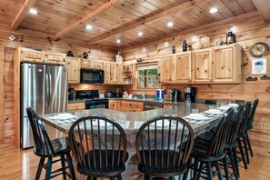 A wooden cabin-style kitchen with a central island, stainless steel appliances, and a dining area with six chairs.