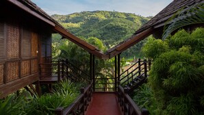 A wooden staircase leading to a building with a thatched roof, surrounded by lush greenery and a view of a hilly landscape. - The Luang Say Lodge (Pakbeng)