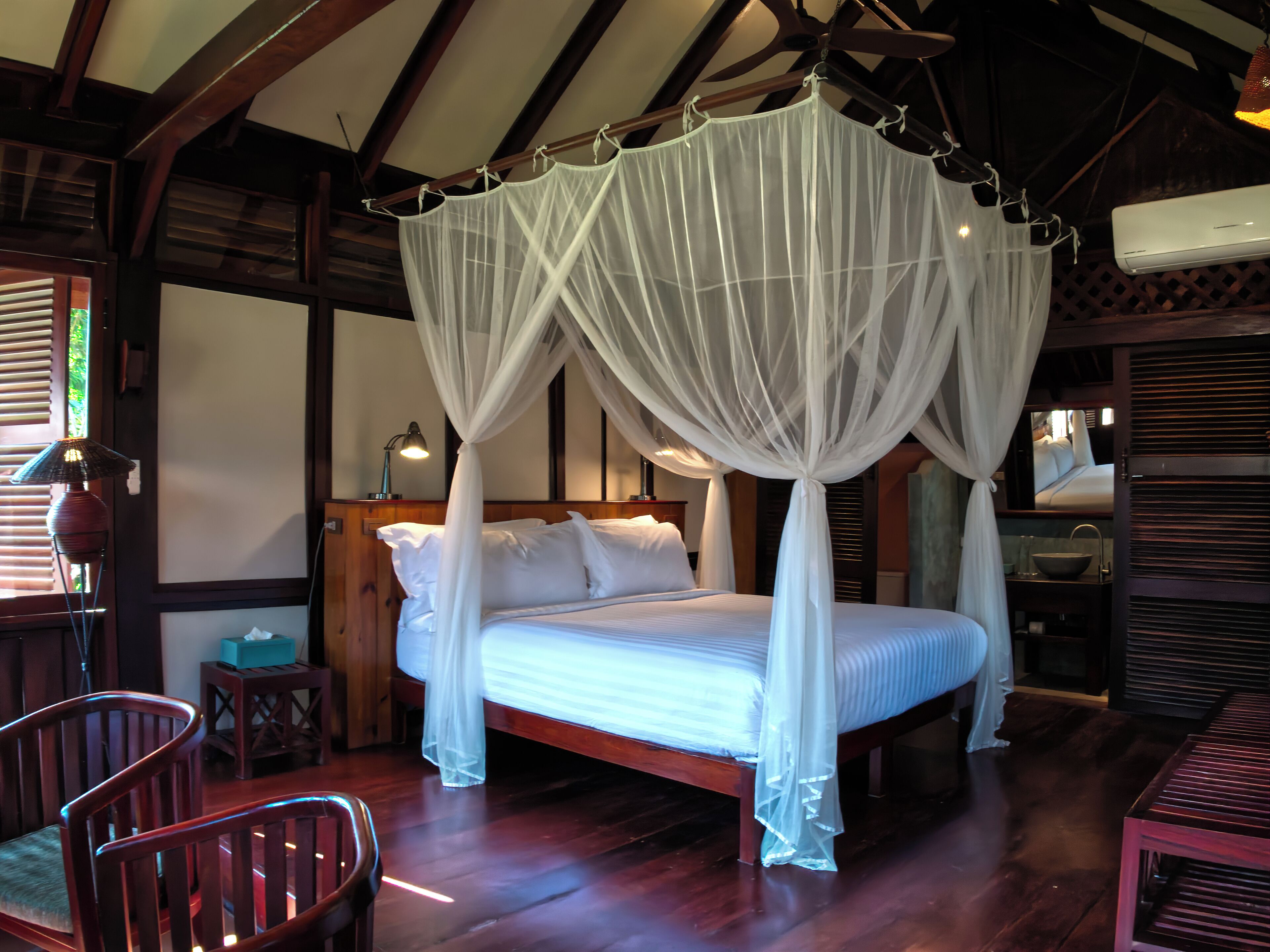 A room with a four-poster canopy bed, wooden flooring, and a wooden-framed ceiling.