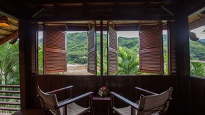 A room with two wooden chairs facing a window with open shutters, overlooking a lush green landscape. - The Luang Say Lodge (Pakbeng)