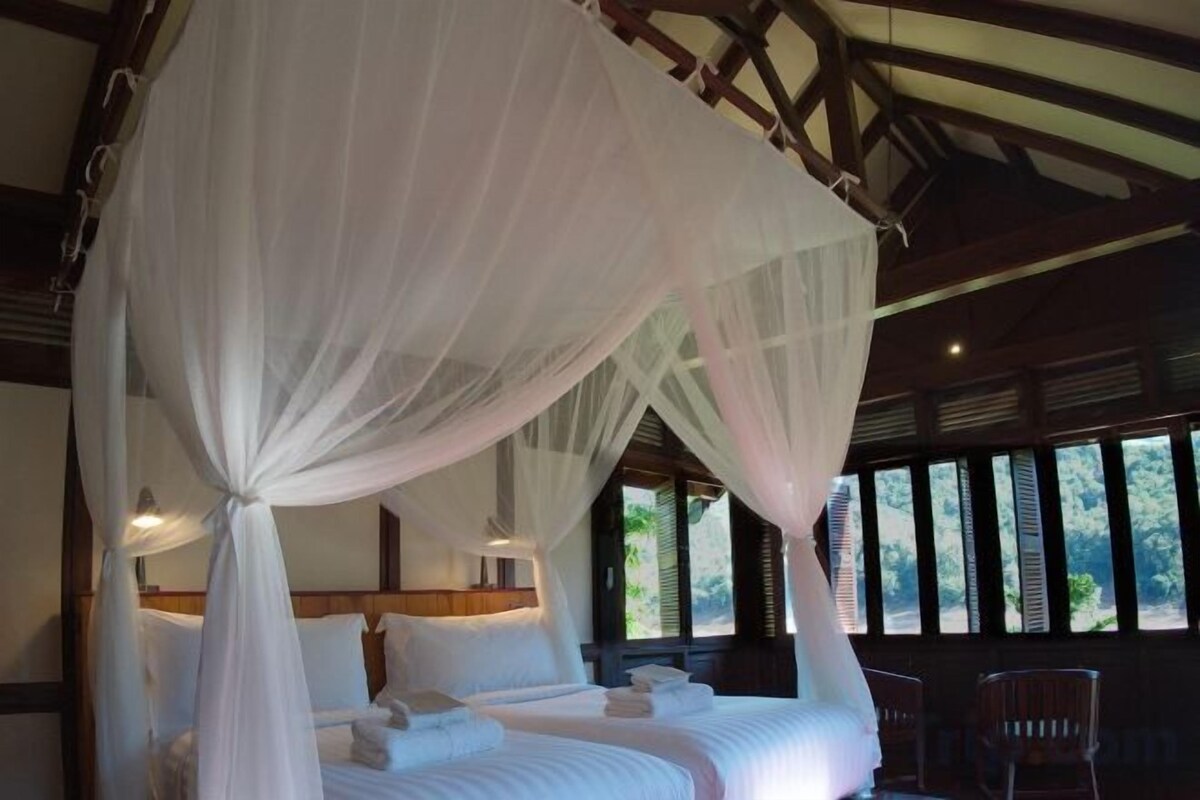 Una cama con dosel, cabecera de madera y vistas al exterior a través de amplios ventanales.