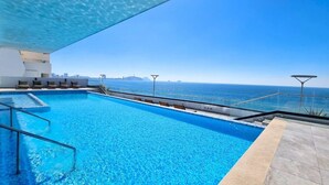 A rooftop swimming pool with clear blue water, a glass balustrade, and a view of the sea and distant cityscape. - ALOHA MAZATLAN (Mazatlán)