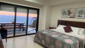 A bedroom with a bed, a nightstand, and a view of the ocean through a sliding glass door. - ALOHA MAZATLAN (Mazatlán)