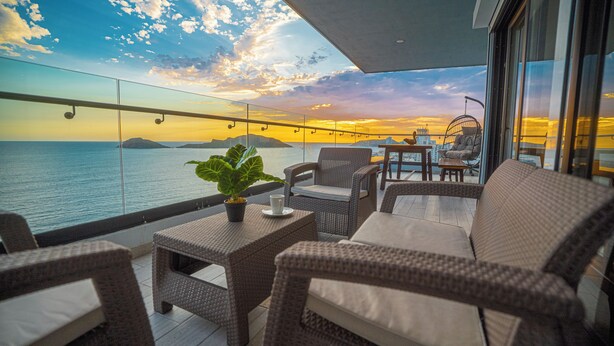 A balcony with wicker furniture, a potted plant, and a view of the sea at sunset. - ALOHA MAZATLAN (Mazatlán)
