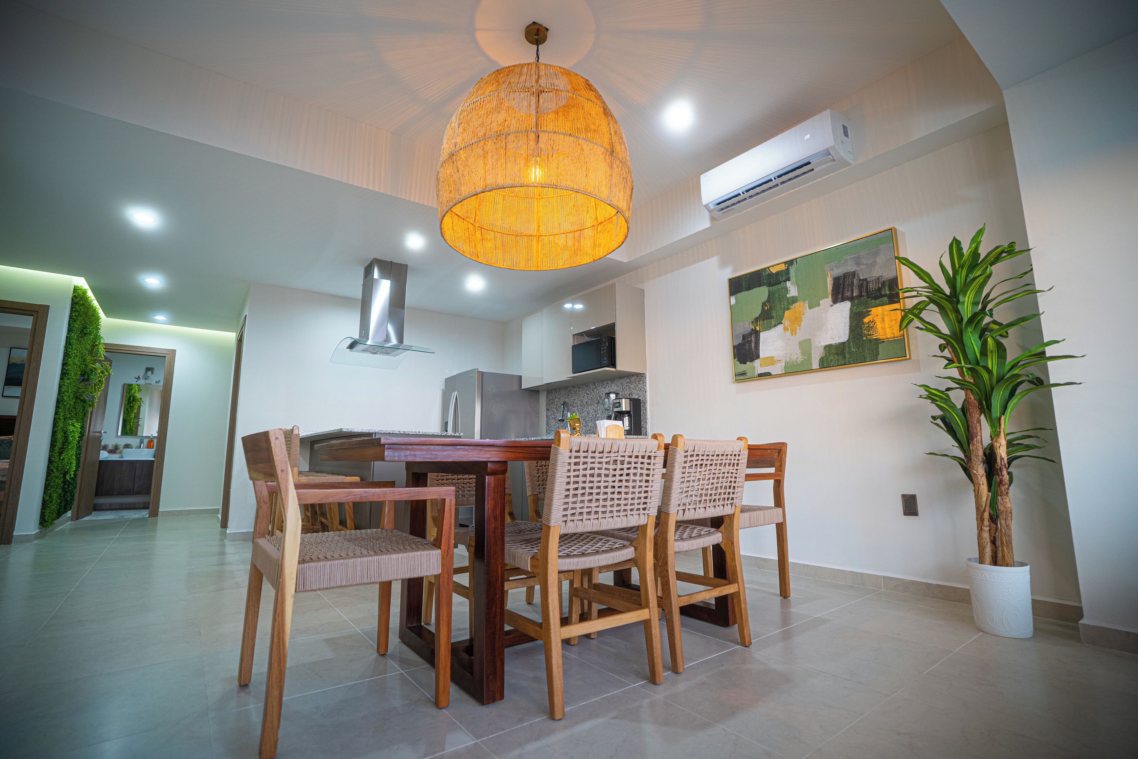 A dining area with a wooden table and chairs, a hanging pendant light, and a potted plant.