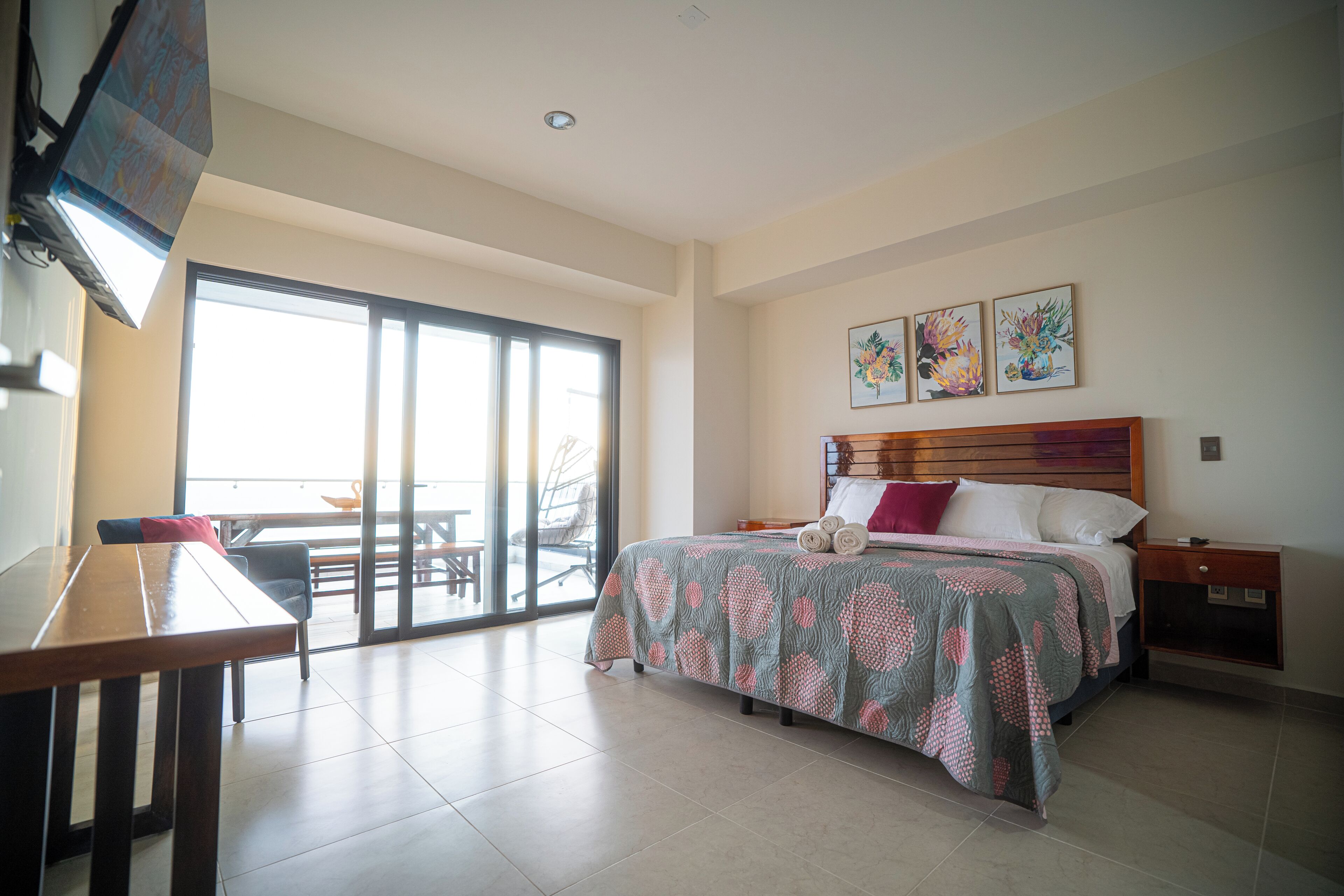 A hotel room with a bed, a desk, and a view of the outdoors through a sliding door.