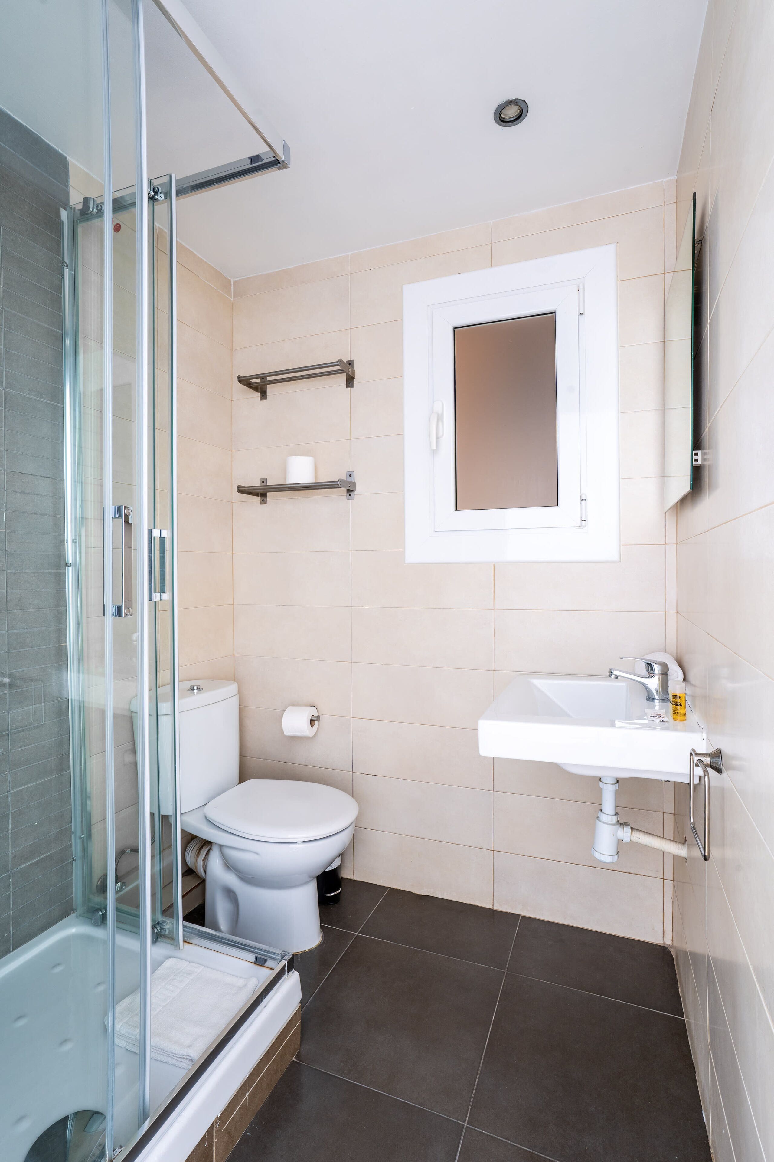 Une salle de bain moderne avec une douche à parois de verre, des toilettes blanches, un lavabo avec un miroir et des murs recouverts de carreaux beiges.