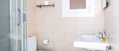 Une salle de bain moderne avec une douche à parois de verre, des toilettes blanches, un lavabo avec un miroir et des murs recouverts de carreaux beiges.