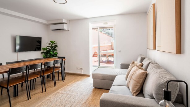 Un salon moderne comprenant un canapé, une table à manger avec des chaises, un téléviseur à écran plat et une grande fenêtre.
