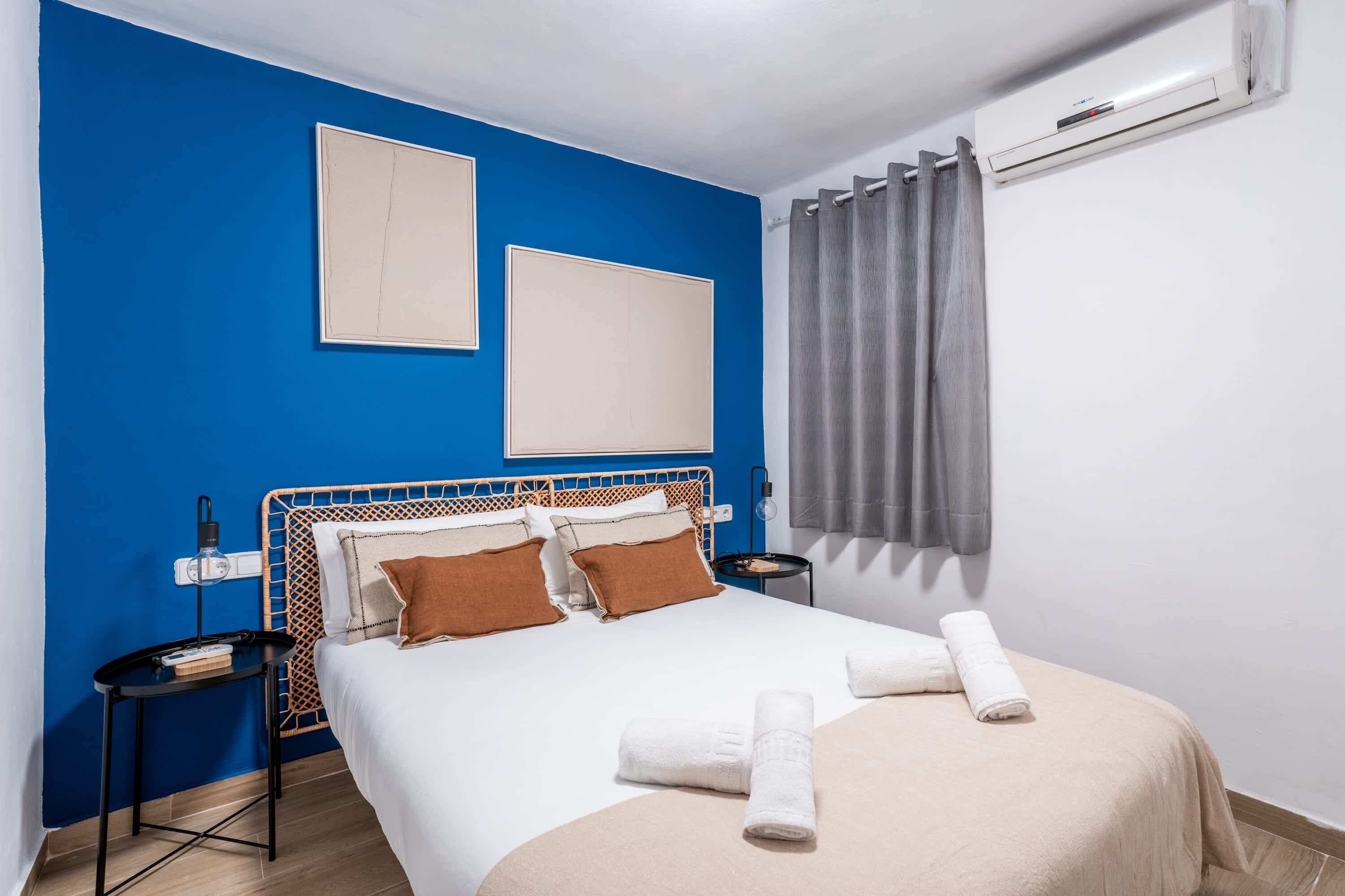 Ein Hotelzimmer mit Bett, Nachttisch, Klimaanlage und einem Fenster mit Vorhängen.