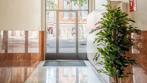 Un hall d’hôtel avec un sol en marbre, une plante en pot et une porte vitrée donnant sur l’extérieur.