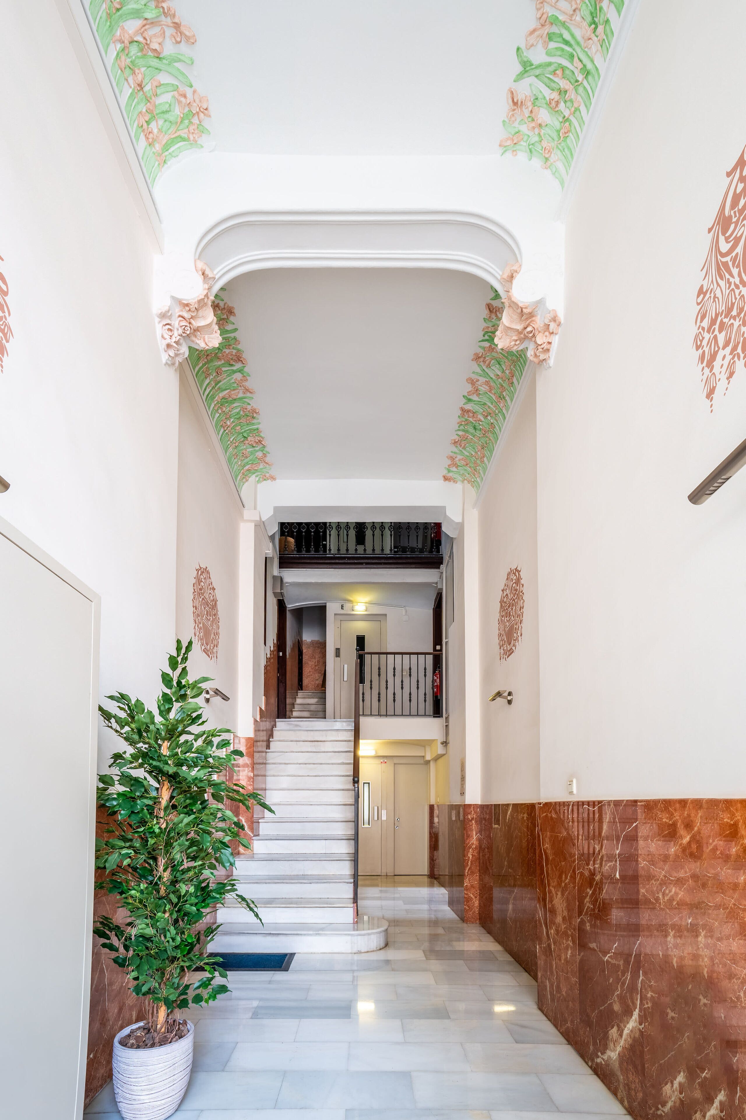 A grand hallway with marble flooring, a potted plant, and a staircase leading to an upper level.