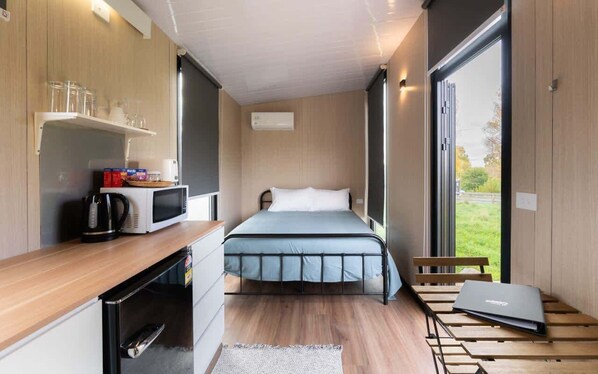 A compact room with a bed, a small kitchenette, a window, and a laptop on a table.