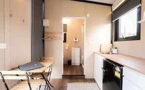 A compact kitchen with a dining area, a small refrigerator, and a window providing natural light. - Weka Pass Cottages 1 by Tiny Away (Waikari)