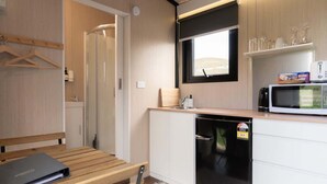 A compact kitchen with a microwave, toaster, and small refrigerator. There is a wooden bench and a table with a laptop. A window provides natural light and a view of the outdoors. - Weka Pass Cottages 1 by Tiny Away (Waikari)