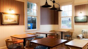 A dining area with wooden tables and chairs, large windows with striped curtains, and wall-mounted picture frames. - Weka Pass Cottages 1 by Tiny Away (Waikari)