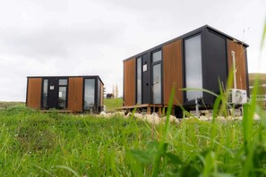 Two modern, wooden cabins with large windows, situated in a grassy field.