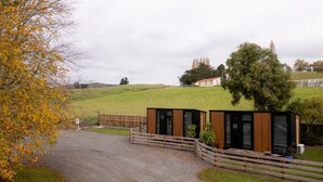 A modern building with a wooden fence and a paved driveway leading to it. - Weka Pass Cottages 1 by Tiny Away (Waikari)