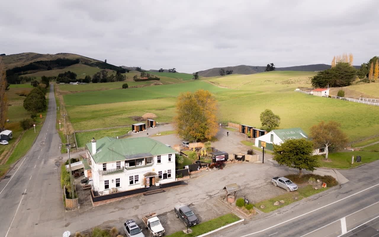 A rural setting with a white building with a green roof, surrounded by open fields and a few trees.