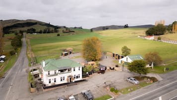 A rural setting with a white building with a green roof, surrounded by open fields and a few trees.