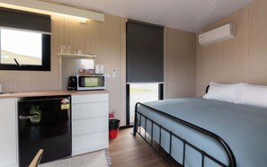 A compact room with a bed, a small kitchenette with a microwave, and a window providing a view. - Weka Pass Cottages 2 by Tiny Away (Waikari)