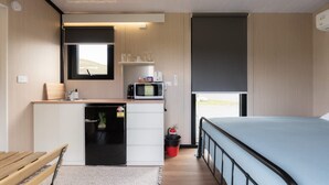 A compact room with a bed, a small kitchenette with a microwave, a sink, and a window.