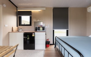 A compact room with a bed, a small kitchenette with a microwave, a sink, and a window. - Weka Pass Cottages 2 by Tiny Away (Waikari)