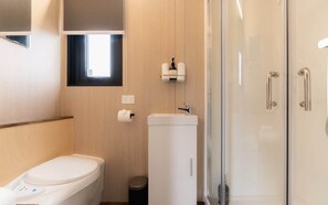 A compact bathroom with a toilet, a sink, a small trash bin, and a glass shower enclosure.