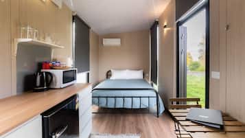 Habitación pequeña con cama, kitchenette, ventana y un ordenador portátil sobre una mesa.