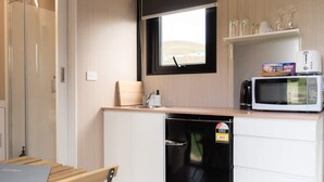 A compact kitchen with a microwave, a small refrigerator, and a window with a view of the outdoors.