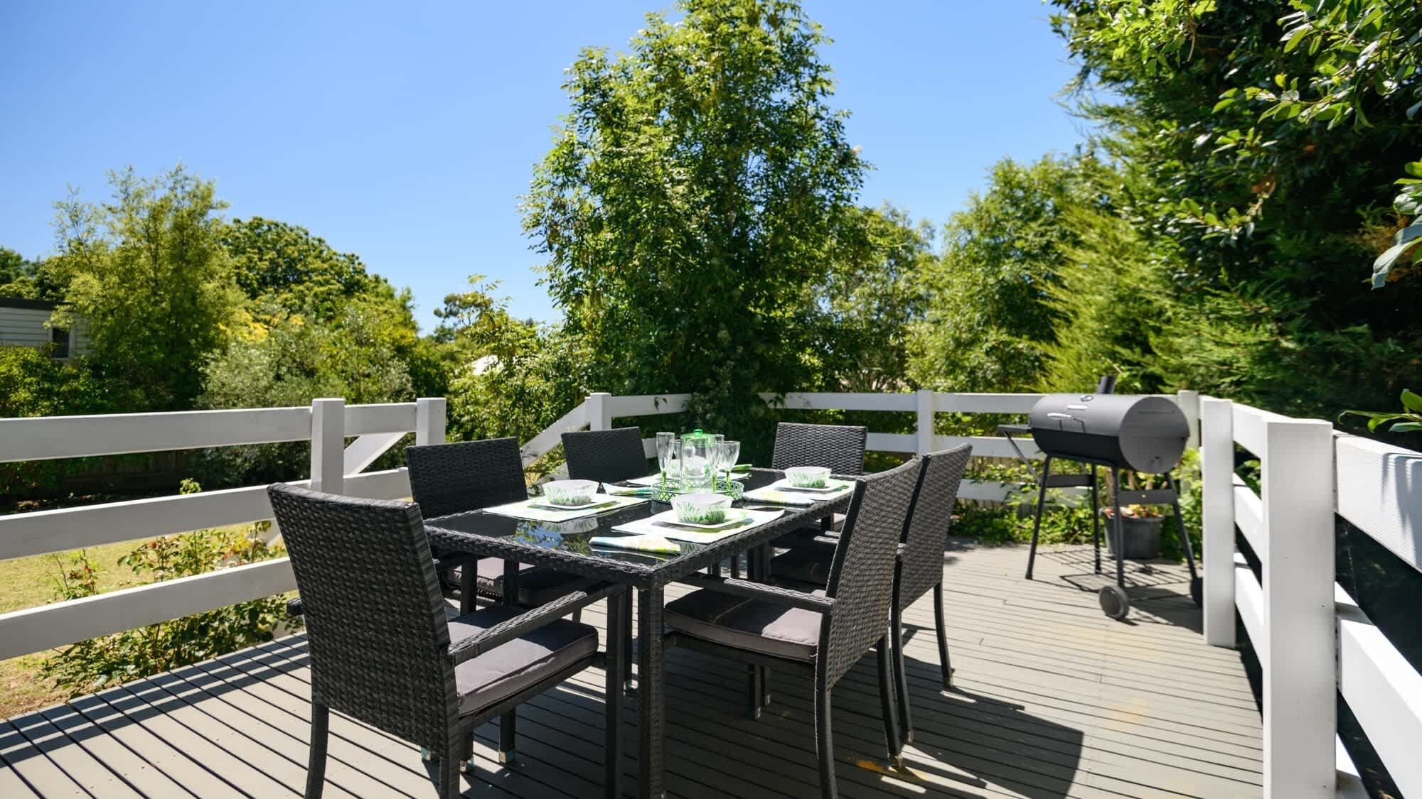 An outdoor deck with a table set for dining, surrounded by wicker chairs, and a grill in the background.