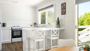A modern kitchen with white cabinetry, a built-in oven, a sink, and a window overlooking greenery. - Savanna Lodge Daylesford (Daylesford)