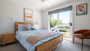 A bedroom with a wooden bed, a nightstand, a chair, and a large window with a view of greenery. - Savanna Lodge Daylesford (Daylesford)
