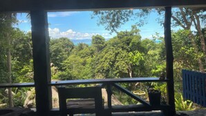 A covered outdoor area with a bench and potted plants, overlooking a lush green landscape and a body of water.