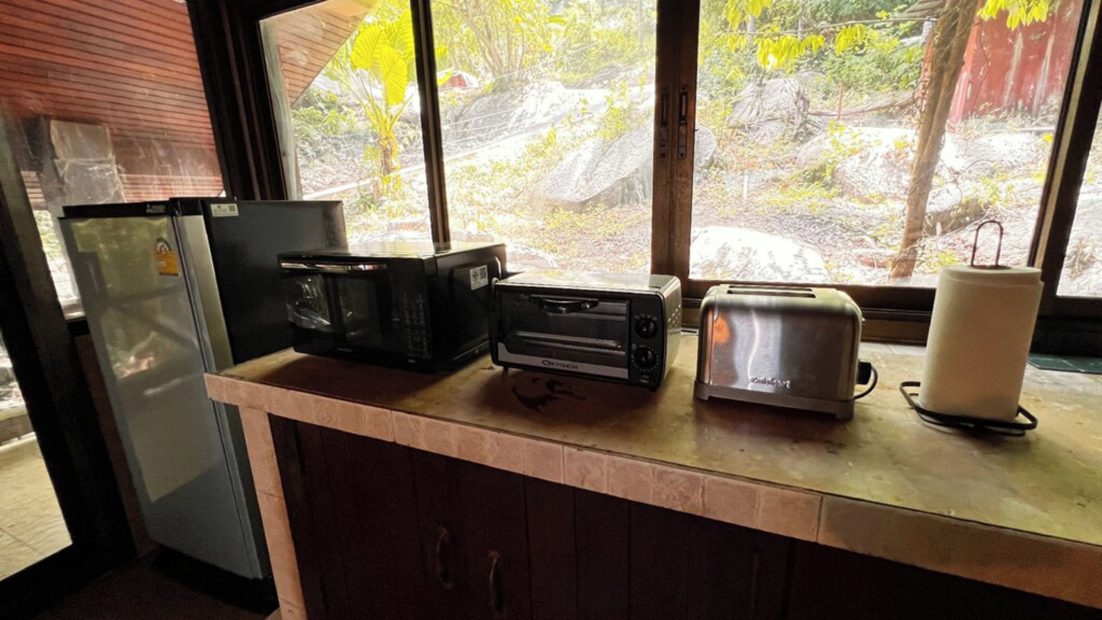 Une cuisine équipée d’un réfrigérateur, d’un four à micro-ondes, d’un grille-pain et d’une fenêtre donnant sur des arbres et des rochers.